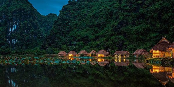 Dãy bungalow mái tranh bên hồ sen dưới chân núi về đêm — Ninh Binh Valley Homestay