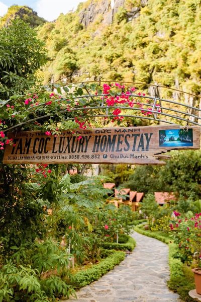 Cổng vào với biển hiệu và lối đi giữa vườn hoa giấy — Tam Coc Luxury Homestay