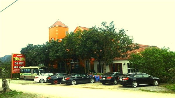 Xe khách và ô tô con đỗ kín sân trước biển hiệu nhà hàng Thăng Long, phía xa là dãy núi đá Ninh Bình